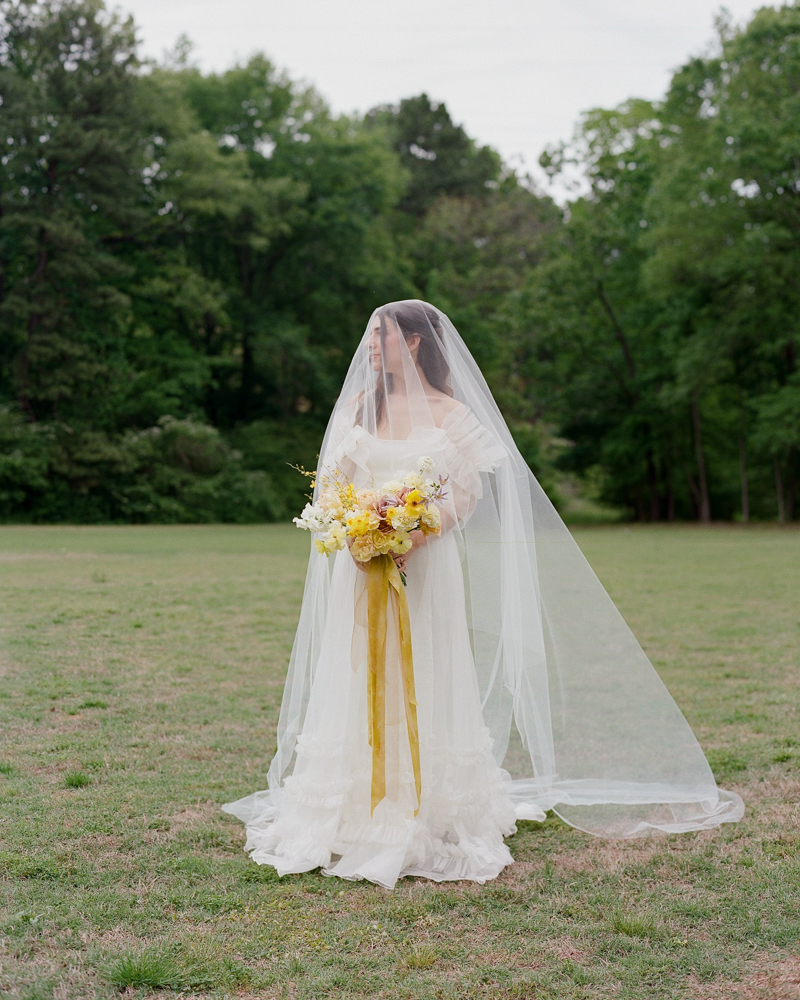 The bride holds her yellow bouquet of flowers with her veil on in a Southern field.