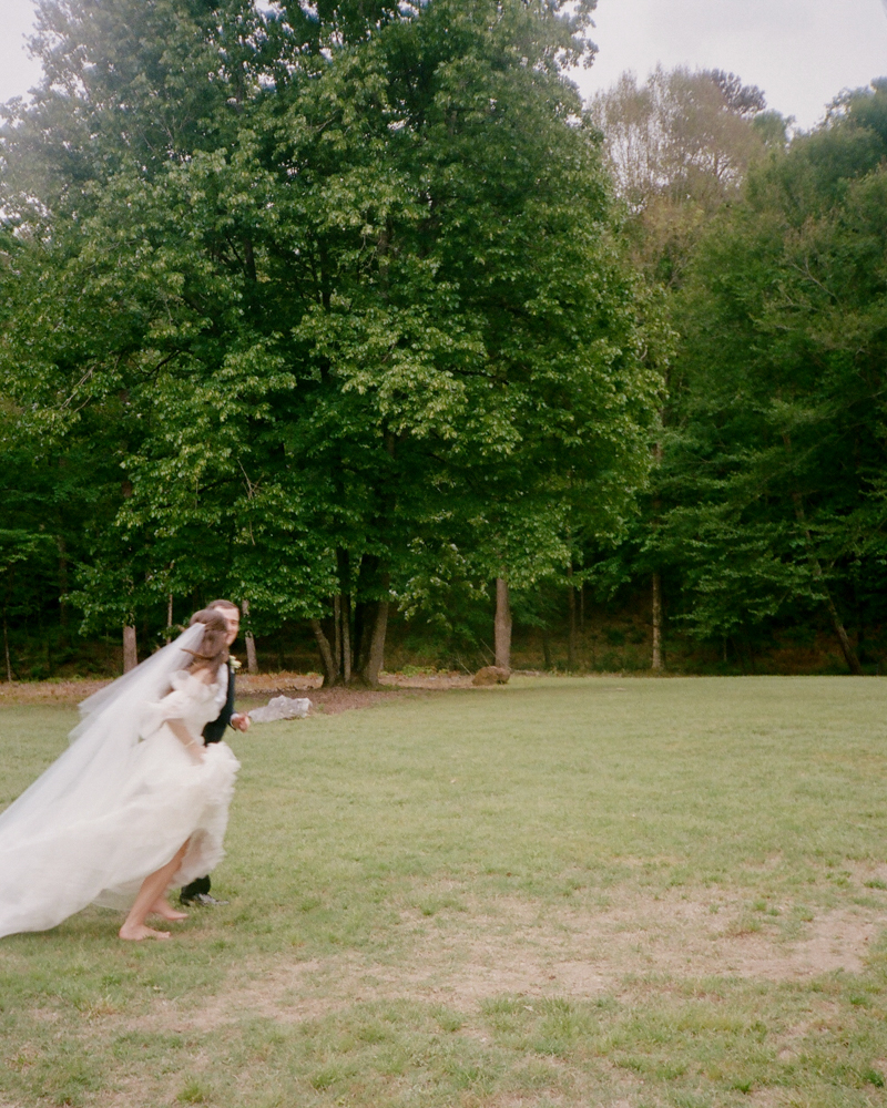 The bride and groom run across a field together on their wedding day in Birmingham, Alabama.