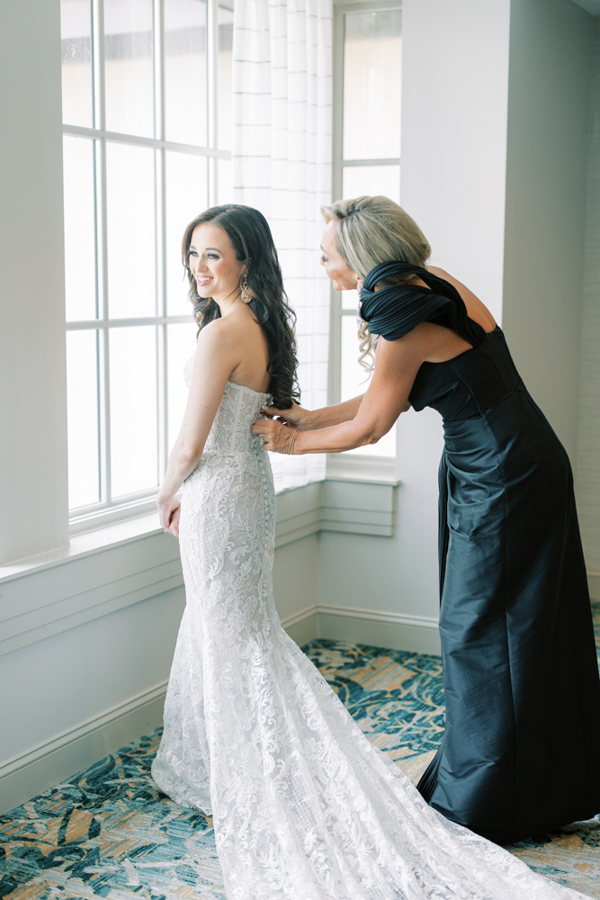 The mother of the bride helps the bride into her wedding dress.