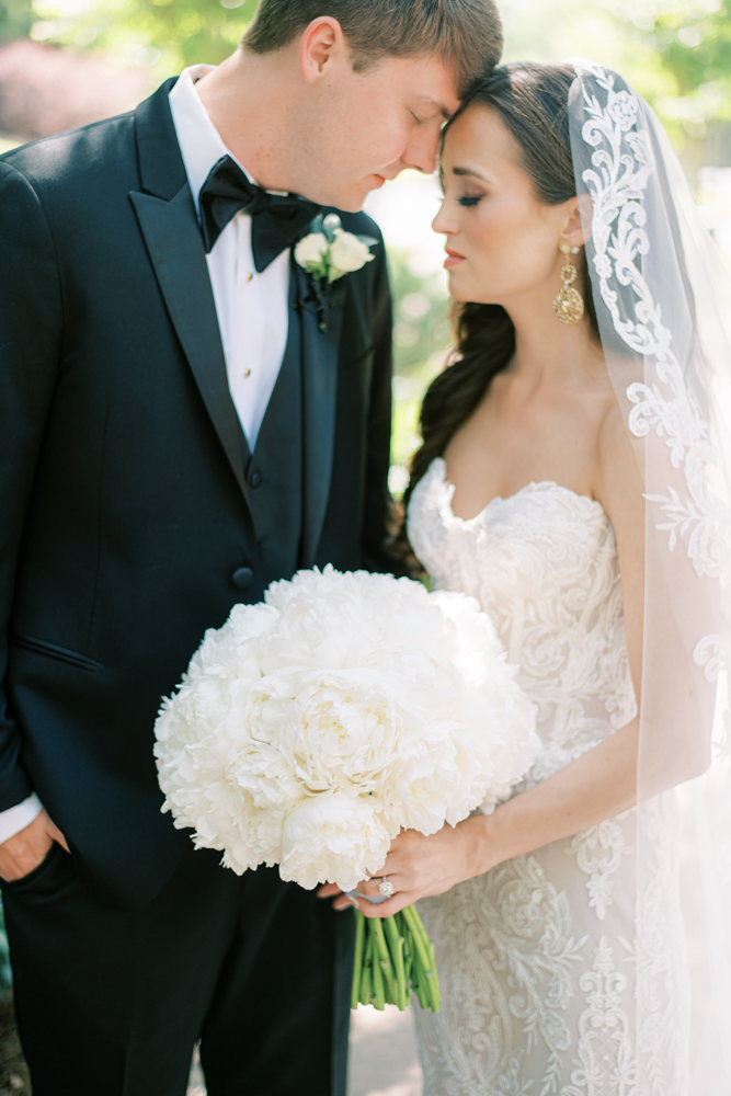 The bride and groom share a moment together while the bride holds a white peony bouquet.