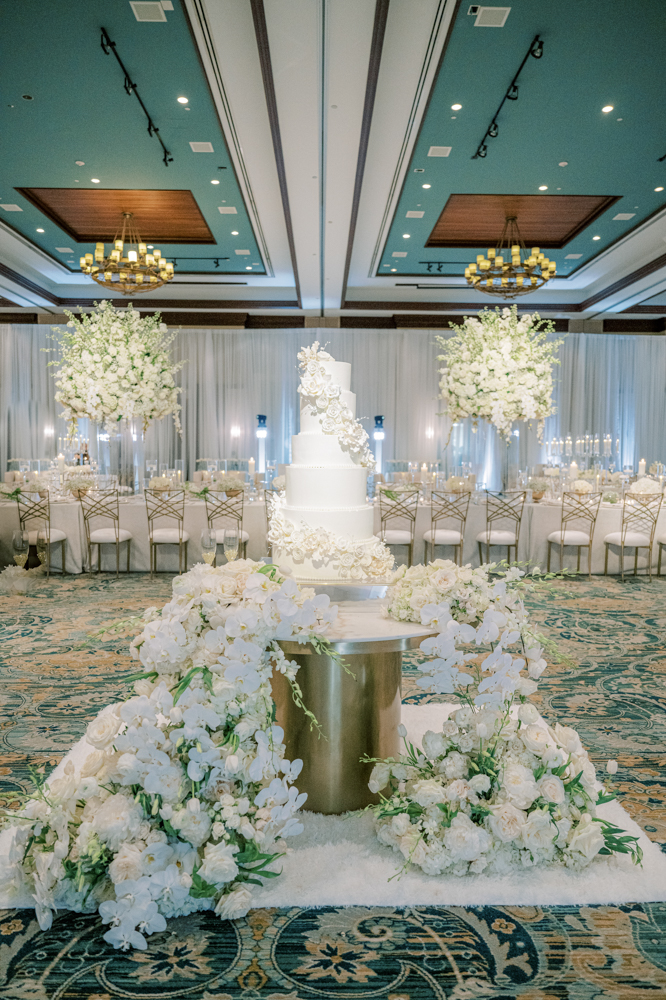 A classic white wedding cake is surrounded by beautiful white flowers in the ballroom of Ross Bridge Resort.