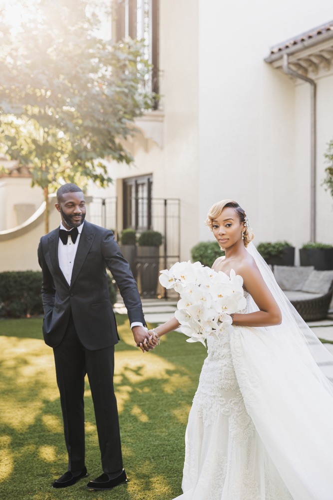 The bride holds a bouquet of white orchids as she walks with her groom, Mayor Woodfin of Birmingham, Alabama.