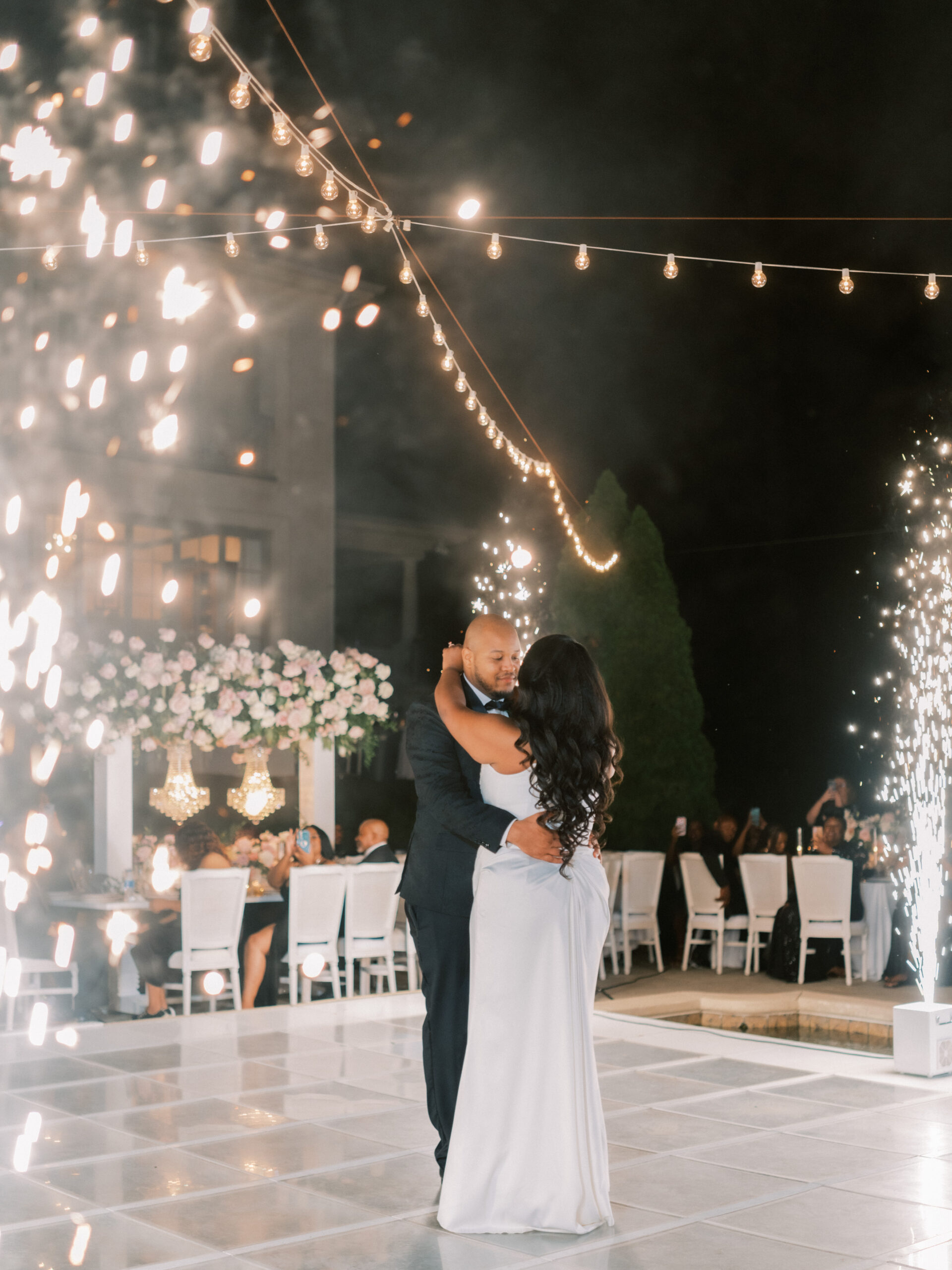 The bride and groom share a first dance as cold sparks go off on the dance floor.