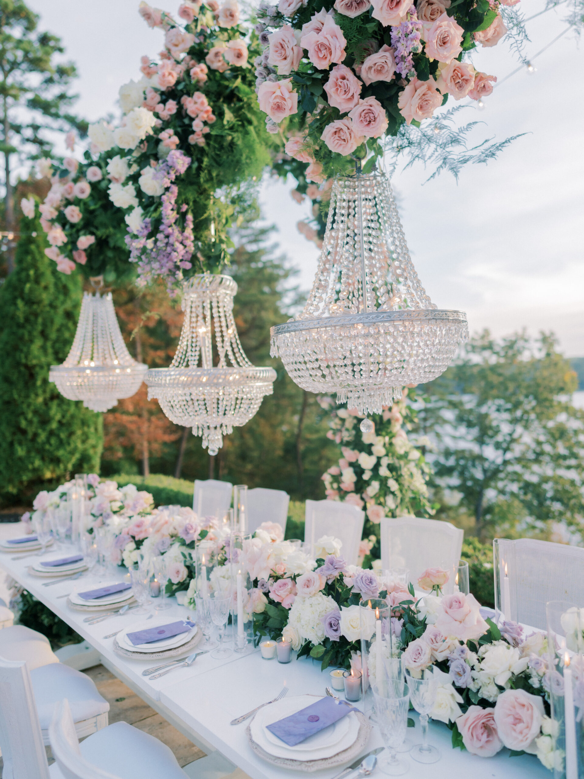 The reception table design has chandeliers and purple flowers.