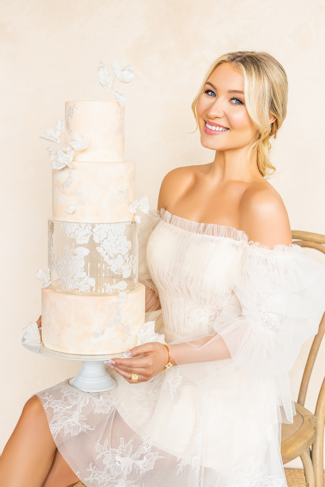 A bride sits holding a wedding cake from Cakes by Kim wearing a short wedding dress from Bella's Bridal.