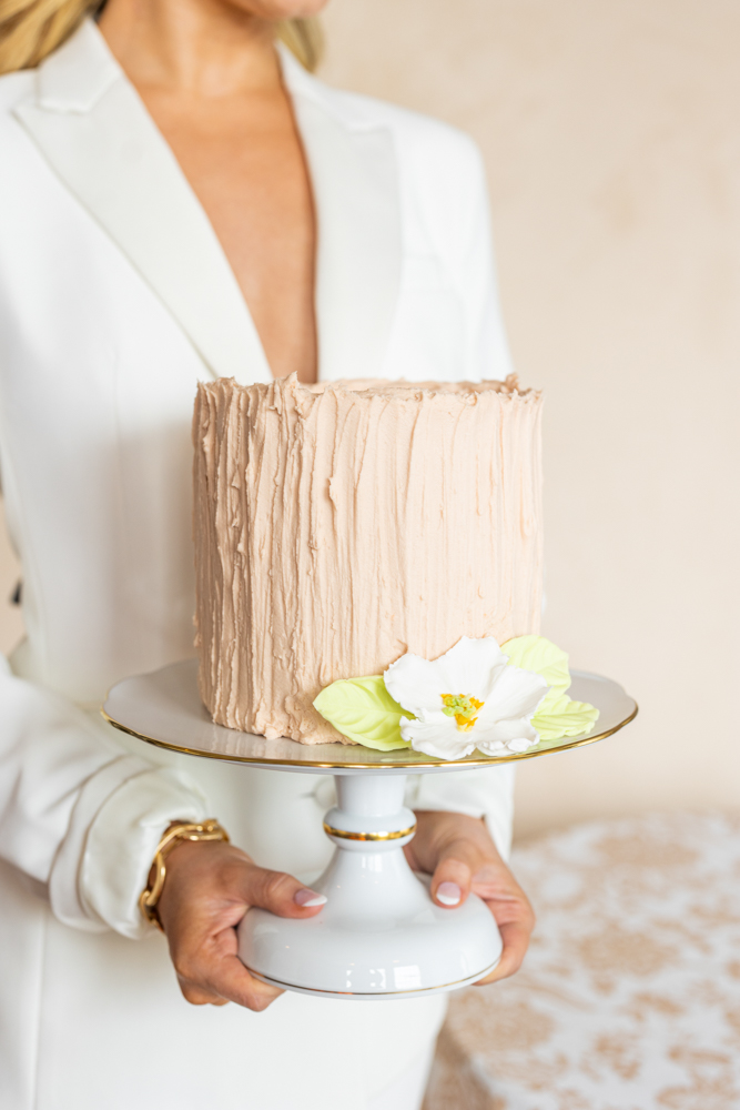 An Alabama bride holds a mini cake on a pedestal while wearing a bridal suit from Bella's Bridal.