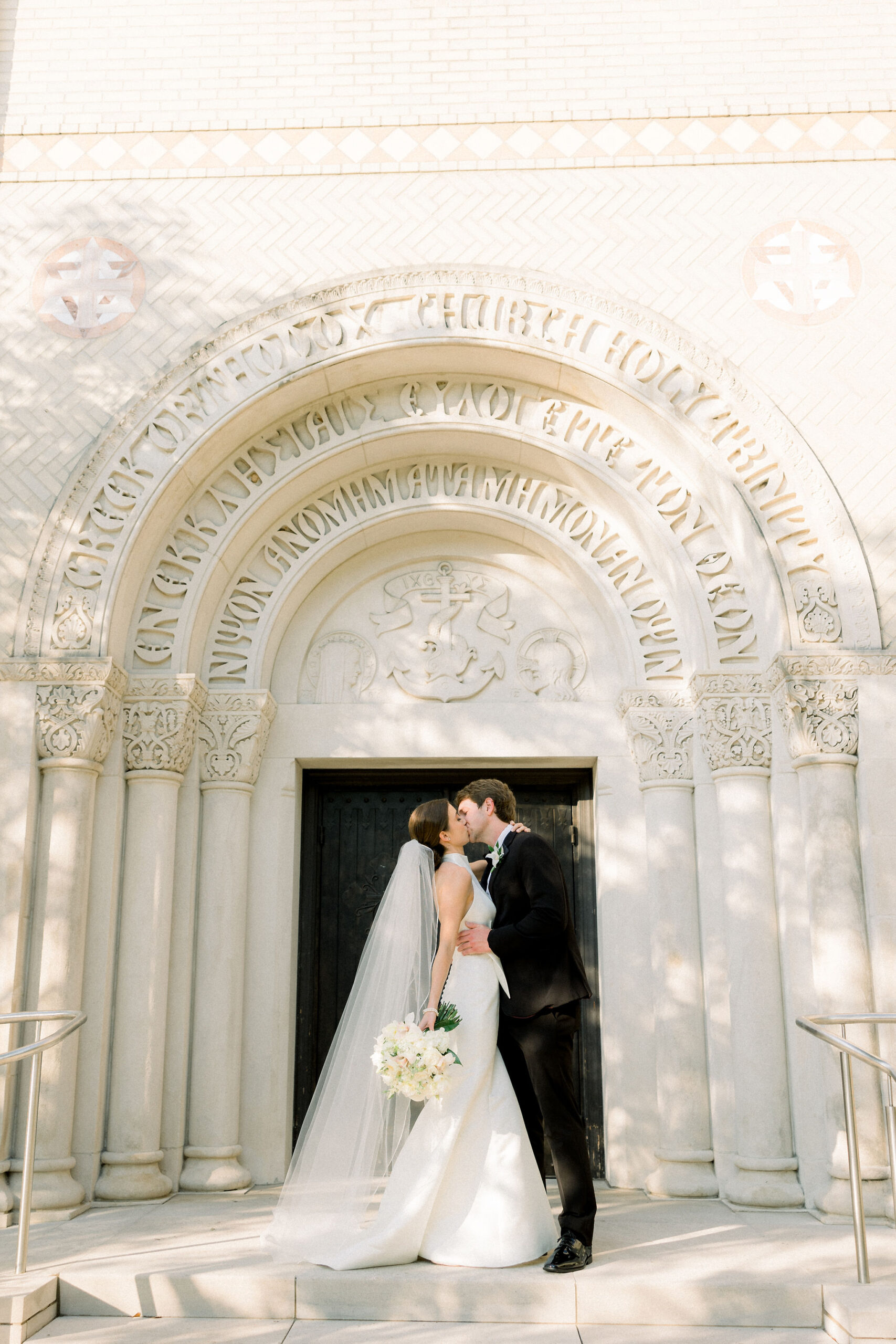 The bride and groom kiss in front of the church at their Southern wedding.