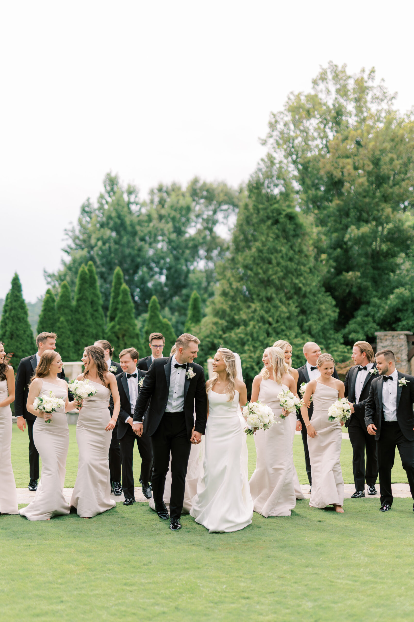 The bride and groom walk with the wedding party walk together across the lawn at Park Crest Event Facility.