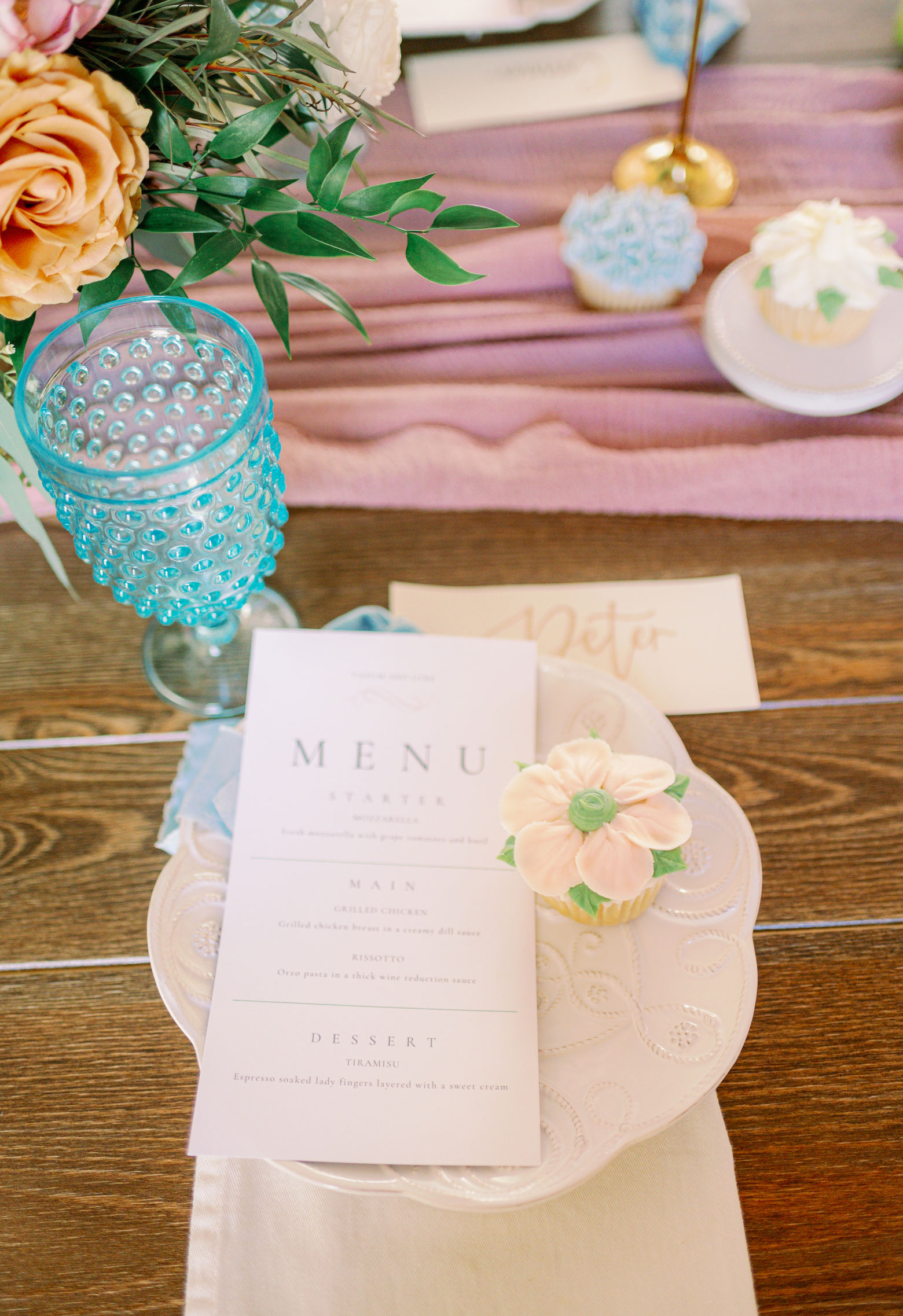 The reception table is set with menus and cupcakes for the wedding.