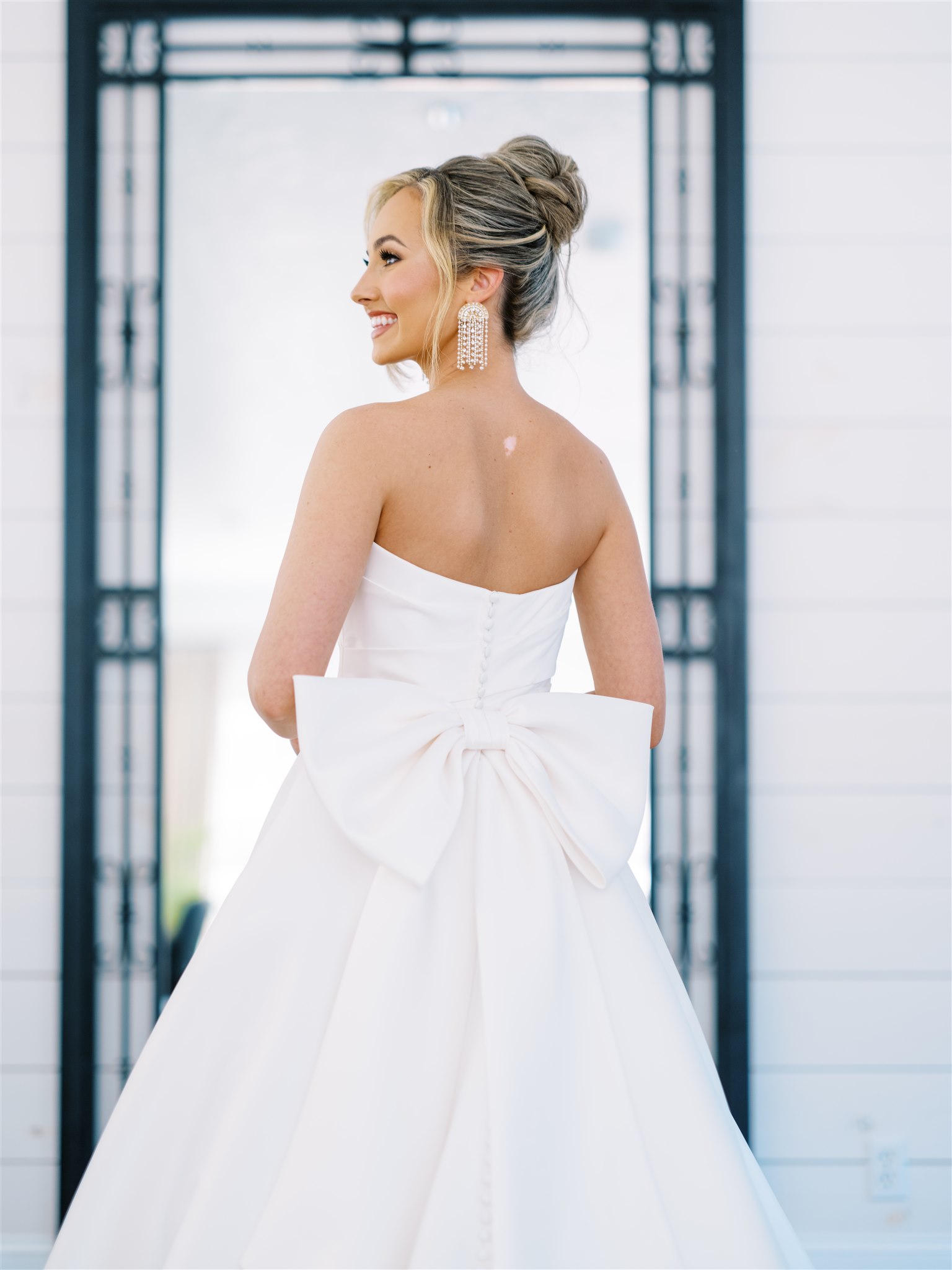 The bride has a large bow on the back of her wedding dress with statement earrings.